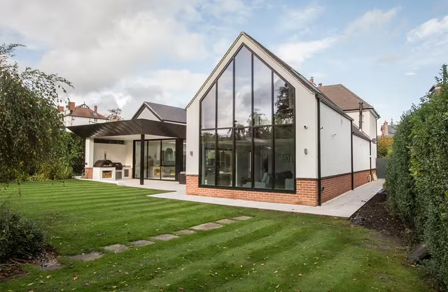 Modern house extension with floor-to-ceiling glass curtain walling and aluminium framing system, brick base, landscaped garden.